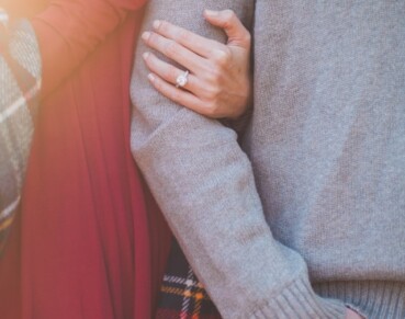 A man and woman link arms. The woman is wearing an engagement ring on her ring finger.