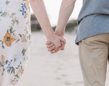 A couple holds hands while walking together on a beach