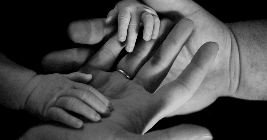 A parent's larger hands are being grasped by a baby's tiny hands.