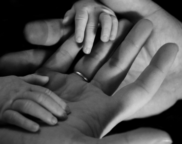 A parent's larger hands are being grasped by a baby's tiny hands.