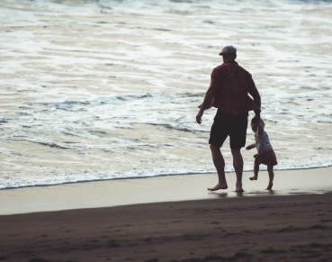 An adult is holding the hand of a child as they stand in front of ocean waves